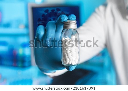 Researcher with oral pill bottle of pharmaceutical antiviral drugs against covid-19 coronavirus. Doctor hand holds antiviral pills and background screen with illustration coronavirus covid-19