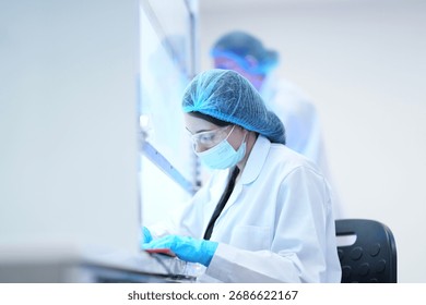 A researcher performs an aseptic technique inside a Class II biosafety cabinet. The sterile environment is critical for cell culture or virology work in a biotechnology lab.