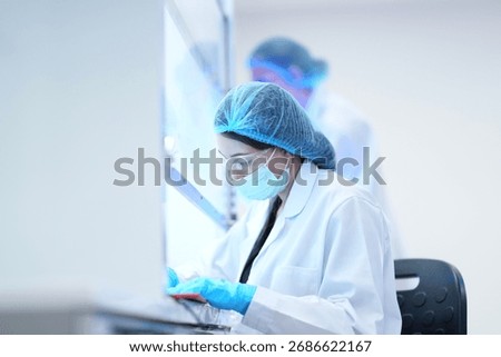 A researcher performs an aseptic technique inside a Class II biosafety cabinet. The sterile environment is critical for cell culture or virology work in a biotechnology lab.