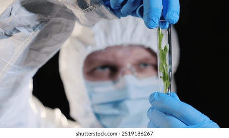 A researcher in a protective suit looks at a test tube with a sample of a plant. Genetic research concept - Powered by Shutterstock