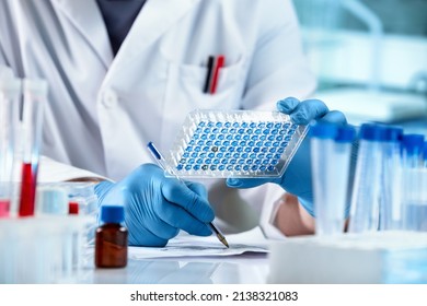 Researcher Sample Analysis and writes down the data result of for elisa analysis. Scientist working with samples panel microplate and registering data for diseases diagnostic in the laboratory
