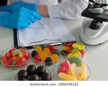 Researcher studies different types of candy on a table while taking notes and using a microscope in a laboratory setting