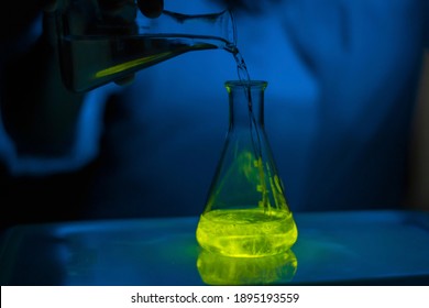 A researcher working with a green fluorescent solution in a glass conical flask in dark biomedical laboratory for drug development