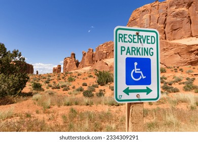 Reserved Parking Sign with Left and Right Arrows and Wheelchair Symbol over Sandstone Rocks in Arches National Park in Moab, Utah, United States. Disabled Parking Area at Popular Tourist Sight