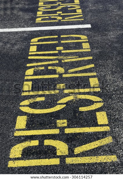 Reserved parking space marked with yellow\
capital letters painted on black asphalt, for concepts of control,\
restriction, benefits