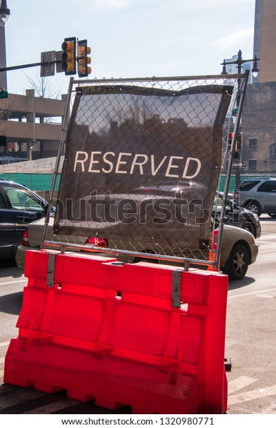Reserved sign seen on a fence near a\
parking spot on city street with cars in\
background