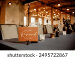 A reserved table sign on a beautifully decorated table at a rustic event venue. The warm lighting and elegant setup create an inviting atmosphere, perfect for weddings and special occasions.