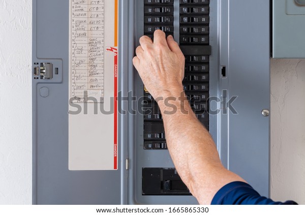 Resetting tripped breaker in residential\
electricity power panel. Male electrician turning off power for\
electrical outlet at circuit breaker\
box.