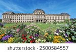 The Würzburg Residence, a Baroque and Rococo masterpiece from the 18th century designed by Balthasar Neumann, seen with wildflowers of various colors in the foreground.