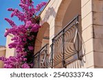 Residential building with balcony and vibrant bougainvillea flowers on facade against blue sky. Coastal villa at summer day. Croatian architecture in coastal town