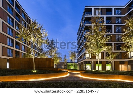 Residential buildings in a European city at night. Modern blocks of flats. Courtyard with vegetation and lighting. Rust metal finish, corten. Underground garage