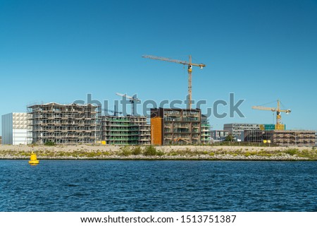 Residential construction on the Northern part of Amsterdam, the Netherlands. Modern waterfront apartment buildings, tower cranes, construction site, river IJ. New houses for sale.