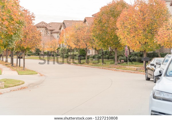 Residential\
Dallas, Texas suburb with American flag on a overcast autumn day.\
Yellow fallen leaves sidewalk, new development residential\
neighborhood with parked car on street in\
USA
