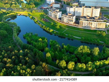 Residential High-rise Buildings In The City Near River. Townhouses And Multi-floor Home, Aerial View. River In City On Sunrise. Multi-storey Residential Building. City Landscape In Green Background.