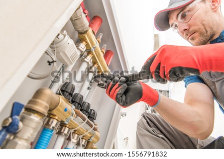 Residential House Floor Heating Valves Adjustment. Plumbing and Heating Technician at Work.