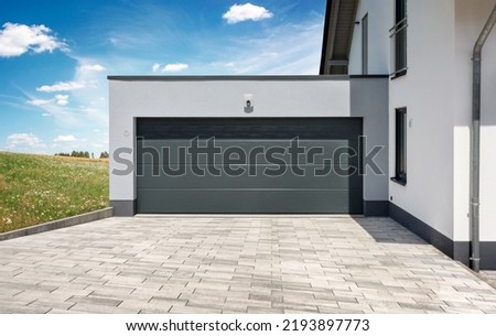 Residential house with modern garage with sectional door in front of landscape in summer