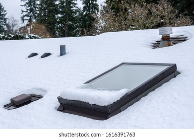 
Residential house rooftop covered in fresh snow, skylight, roof vents, evergreen trees
