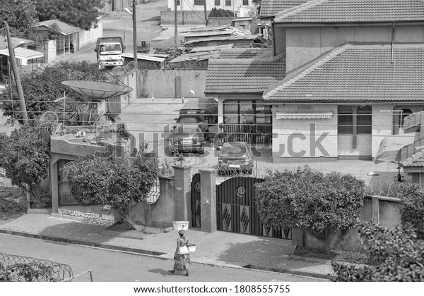 Residential houses and yards with cars.\
African lifestyle. Woman walks along the road. Black and White\
Photography. Ghana, Accra, Tema – January 17, 2017  \
