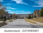 Residential street with speed limit leading down a steep hill row of two-story houses, new development subdivision neighborhood with upscale homes suburbs Atlanta, Georgia, USA. Sunny cloud blue sky