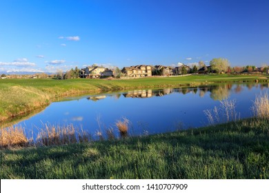 Residential Suburban Lake With Homes Along A Golf Course In Broomfield, Colorado In Spring With The Snow On The Mountains