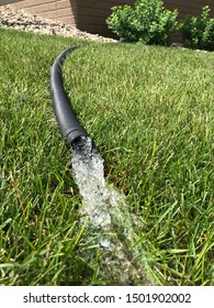 Residential Sump Pump Discharging Water From The End Of A Flexible Black Hose With House Visible In Background