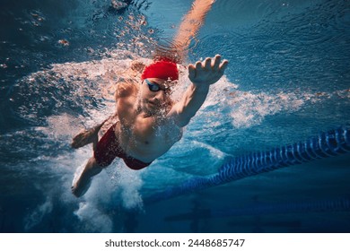 Resilience and strength. Concentrated young man in red cap and goggles in motion, swimming in pool, training. Concept of professional sport, health, endurance, strength, active lifestyle - Powered by Shutterstock