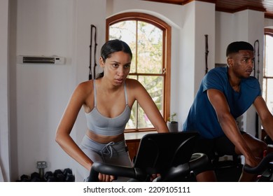 Resilient Young Biracial Woman And Black Man Using Exercise Bike At The Gym