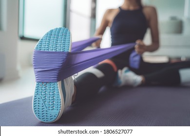 Resistance band exercise at home. Woman doing pilates workout using elastic strap pulling with arms for shoulder training on yoga mat indoors.