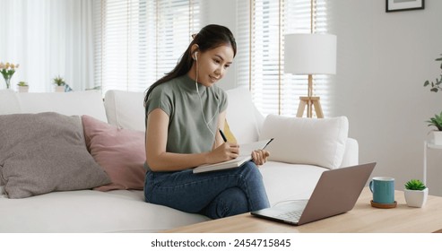 Reskill upskill for young adult talent workforce remote work at home hybrid workplace. Asia woman happy smile sit at sofa couch learn online study MBA video call share plan idea write note on tablet. - Powered by Shutterstock