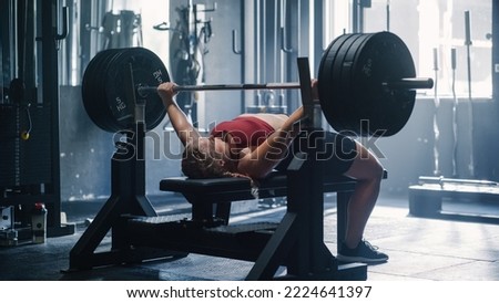 A Resolute Female Bodybuilder Training Alone in a Hardcore Dark Gym Doing Bench Press Exercises. A Strong Woman Lifting Extremely Heavy Weights on a Barbell and Working Out