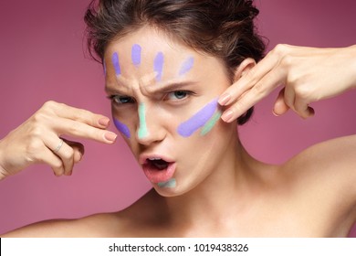 Resolute woman doing makeup using concealer. Photo of beautiful brunette woman on pink background. Skin care concept
