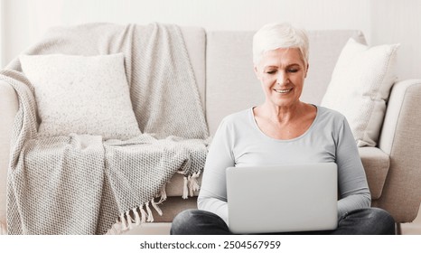 Resourceful mature smiling woman sitting on floor and using laptop at home, copy space - Powered by Shutterstock