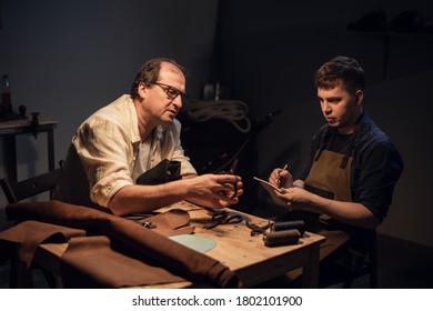 a respectable elderly shoemaker conducts a master class for a young boy on making shoes by hand in a special workshop - Powered by Shutterstock