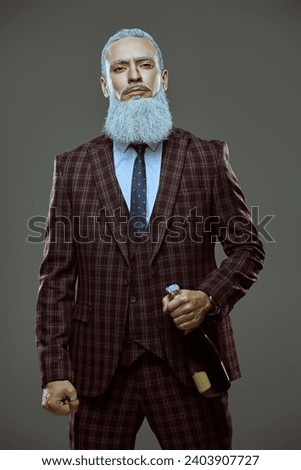 A respectable man with a gray hairstyle and a beard in Japanese style, dressed in an elegant suit, looks calmly and confidently into the camera. Gray studio background. Business concept.