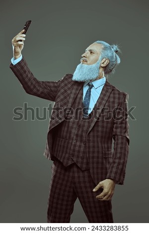 A respectable man with a gray hairstyle and a beard in Japanese style, dressed in an elegant suit, makes selfie. Gray studio background. Business concept.