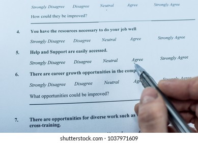 Respondent Holding A Pan In A Hand And Answeing Questions In Employee Survey. Questions Relating To Managerial Practices, Corporate Culture, Career Growth, And Professional Relationships. Close-up