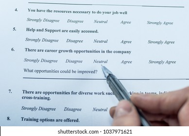 Respondent Holding A Pan In A Hand And Answeing Questions In Employee Survey. Questions Relating To Managerial Practices, Corporate Culture, Career Growth, And Professional Relationships. Close-up