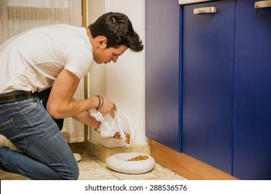 Responsible Attractive Young Man Filling Pet Bowl With Dry Food For Cat Or Dog In Kitchen