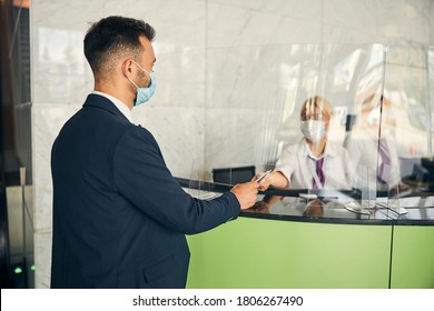 Responsible Male Traveler Wearing A Mask Giving His Passport To An Airport Staff Member