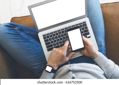 Responsive design. Man sitting on couch with laptop and smartphone, and smartwatch on wrist