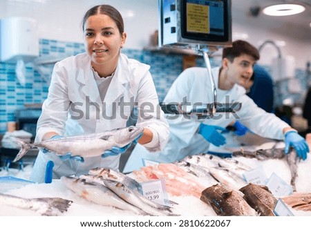 Responsive shop assistant keeping in hands fresh bonito fish in fish store