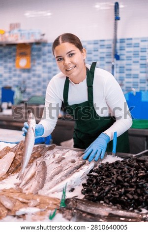 Responsive shop assistant keeping in hands fresh lucet fish in fish store