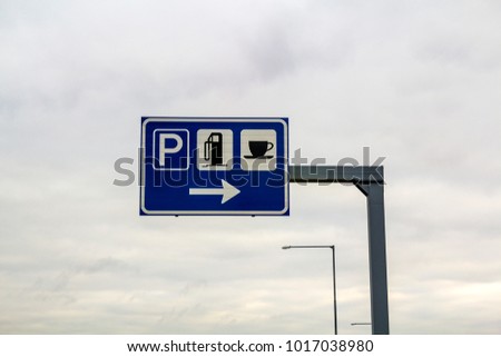 Rest area sign on a pole on freeway road. Signs for parking, gas petrol station and coffee food store.