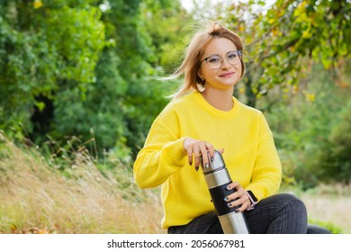 Rest in the autumn in the forest a woman 30-35 years old in glasses looks directly into the camera with a thermos in a cozy yellow sweater outdoors bokeh idyllic nature  - Shutterstock ID 2056067981