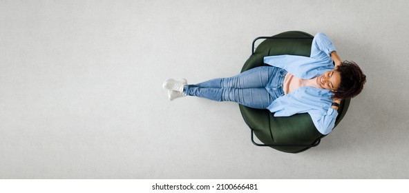 Rest Concept. Above top view of happy black lady sitting on bean bag at home in living room. Cheerful casual woman relaxing on sofa leaning back, enjoying free time, banner panorama, free space mockup