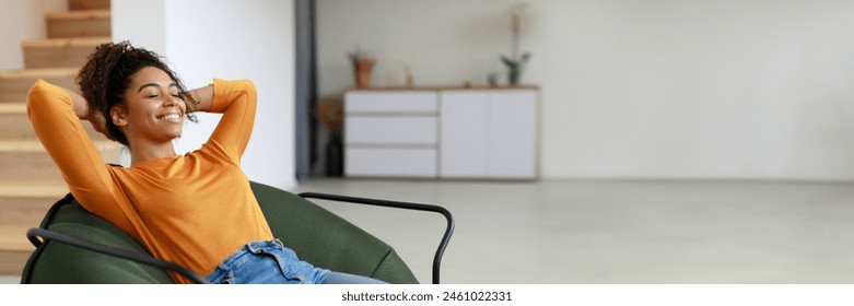 Rest Concept. Happy black lady sitting on comfortable bean bag at home in living room. Cheerful casual woman with closed eyes relaxing on sofa, leaning back, panorama with copy space - Powered by Shutterstock