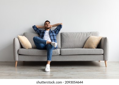 Concepto de descanso. Feliz hombre de Medio Oriente sentado en un cómodo sofá en casa en la sala de estar. Un hombre alegre e informal se relaja en el sofá, se sienta de vuelta, disfruta del tiempo libre del fin de semana o de un descanso del trabajo