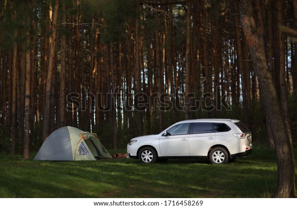 Rest in the forest with a tent, a car is parked\
nearby. Early morning in the forest. Camping in the woods with a\
tent and a car.