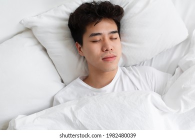 Rest, Lazy, Relax, Sleep At Home In Free Time On Weekends. Be Safety During Covid-19 Quarantine. Tired Millennial Asian Man Asleep, Lying On White Bed In Bedroom, Top View, Copy Space, Close Up