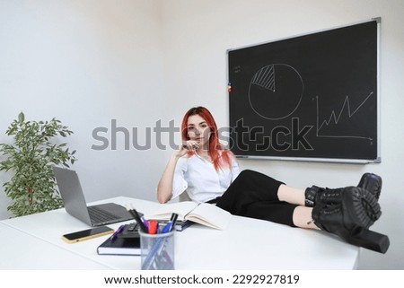 Rest in the office. A woman is sitting at her workplace with her feet on the table. Relaxed and calm at work